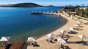 A beach with clear water, sun loungers, umbrellas, and a pier extending into the sea. - Biblos Beach Resort Alaçatı (Cesme)