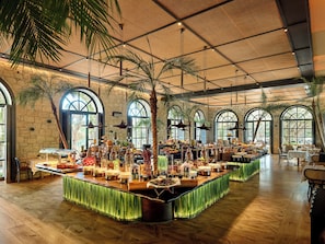 A spacious indoor area with a long buffet table, arched windows, and a high ceiling.