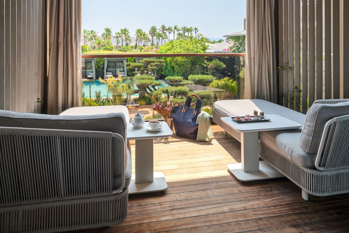 Un área de estar moderna al aire libre con vista a una piscina, que incluye una mesa con tetera y pasteles, y dos sillas.