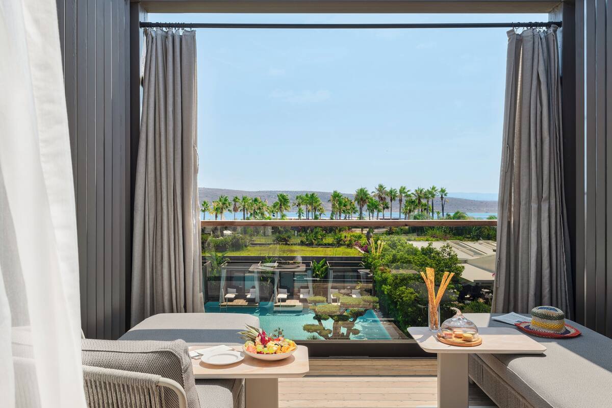 Un balcón con piscina, mobiliario y vistas a palmeras y un paisaje lejano.