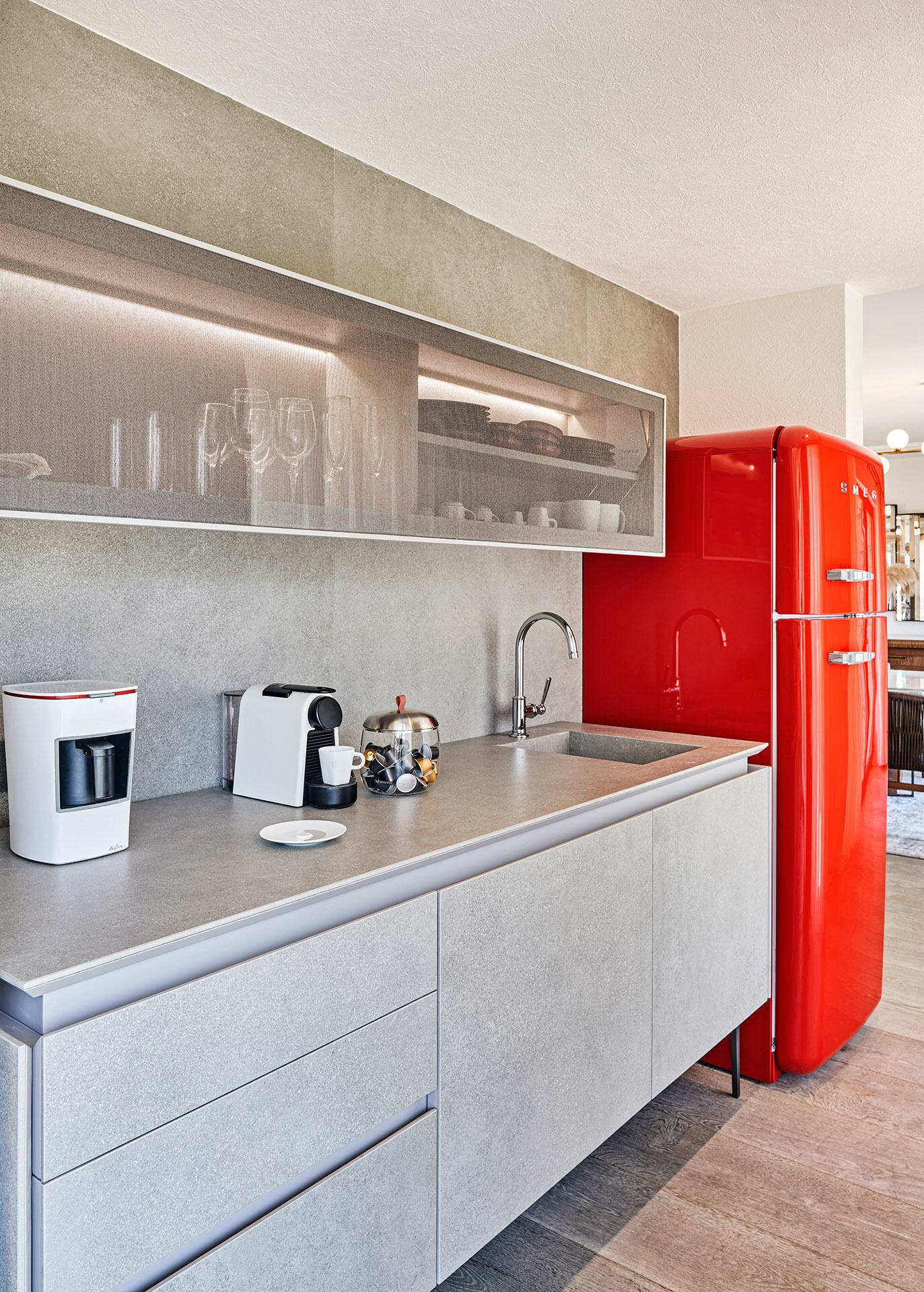 A modern kitchen with a grey countertop, a red refrigerator, a coffee machine, and a kettle.