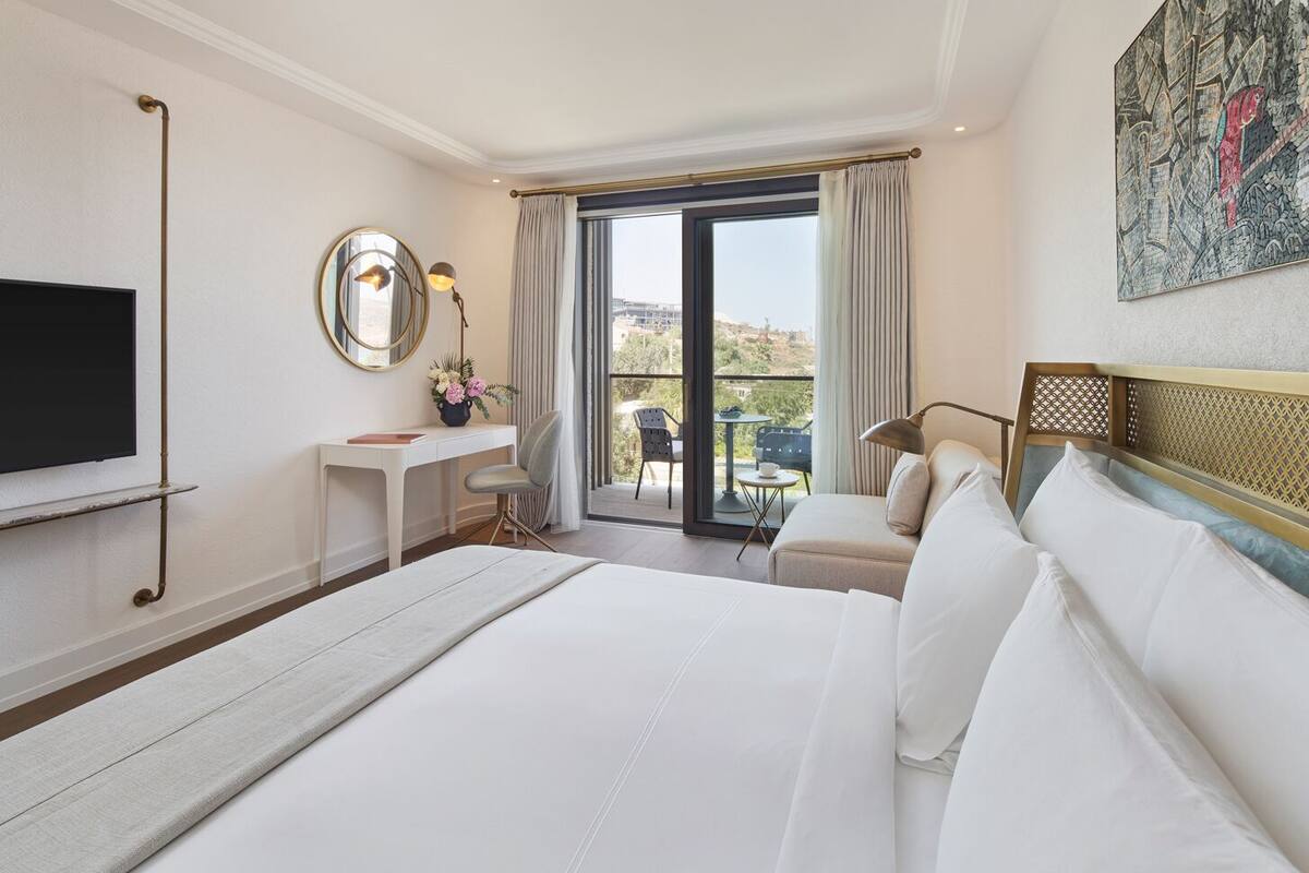 Habitación de hotel con una cama grande, un escritorio, una silla, un televisor y un balcón con vistas.