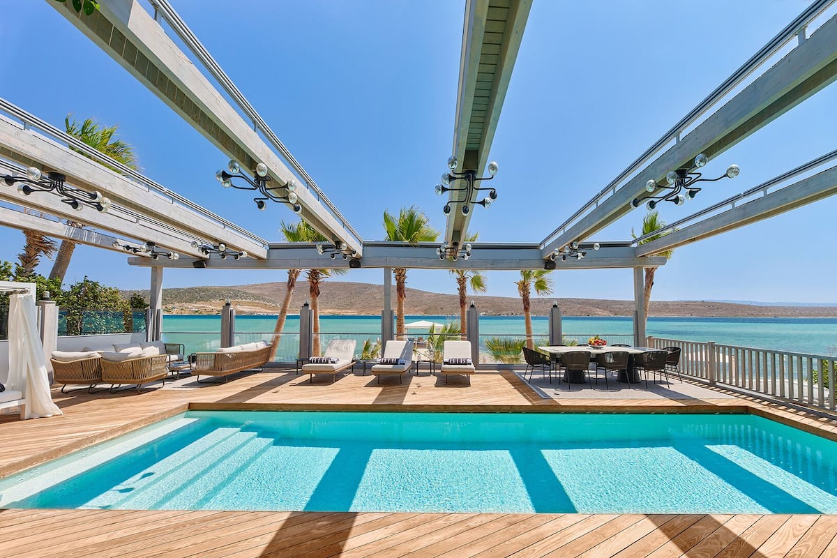 Zona junto a la piscina con sillones de descanso, una mesa y vista al mar.
