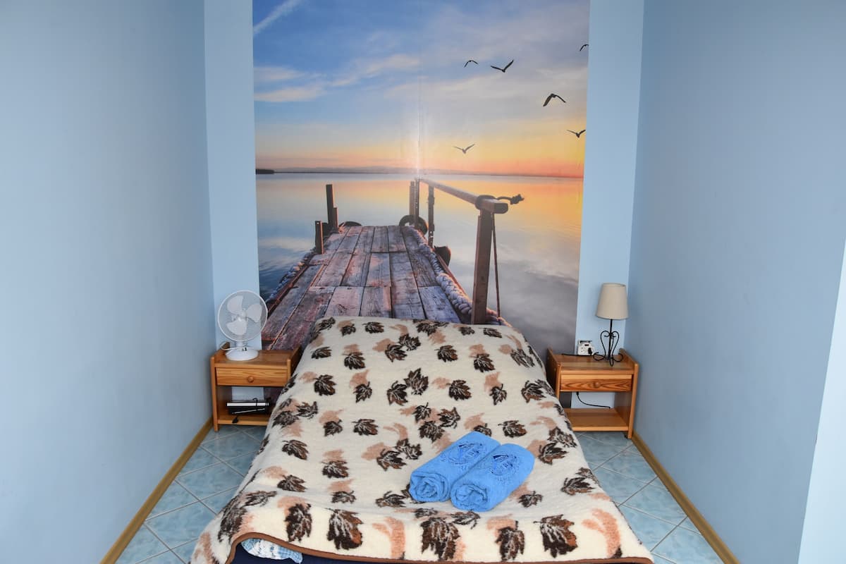 Un dormitorio con una cama, una mesita de noche, un ventilador y una lámpara.