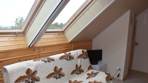 A bedroom with a sloped ceiling, a bed with a floral blanket, a television, and a power outlet. - Agroturystyka u przyjaciol Soni (Zlocieniec)