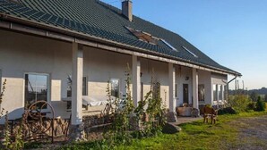 A single-story house with a sloped roof, a front porch with a bench, and a stone wall in the foreground. - Agroturystyka u przyjaciol Soni (Zlocieniec)