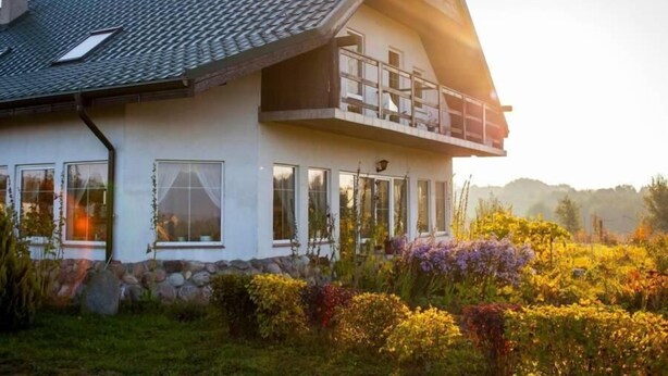 A two-story house with a sloped roof, large windows, and a balcony. - Agroturystyka u przyjaciol Soni (Zlocieniec)