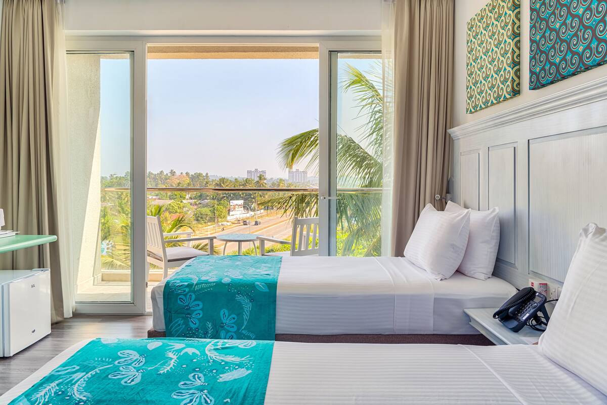 A hotel room with a bed, a desk, and a view of the city through large windows.