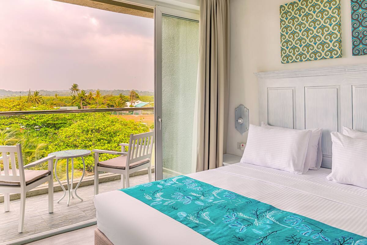 A hotel room with a balcony, a bed with white bedding, a teal throw, and two patterned wall art pieces.