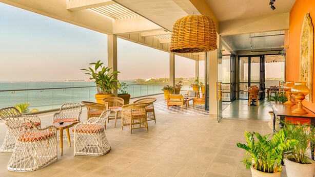 A spacious outdoor seating area with wicker chairs and tables, potted plants, and a view of the sea. - Fairway Sunset (Galle)