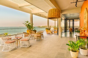 A spacious outdoor seating area with wicker chairs and tables, potted plants, and a view of the sea. - Fairway Sunset (Galle)