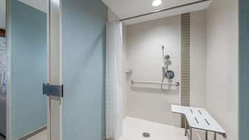 A modern bathroom with a glass partition, a shower with a grab bar, and a white bench.