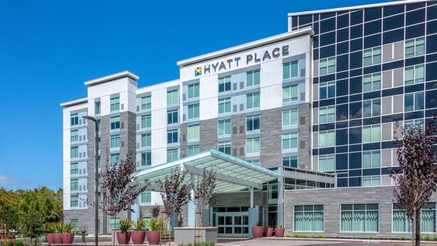 A modern Hyatt Place hotel with a glass facade, a covered entrance, and a landscaped driveway.