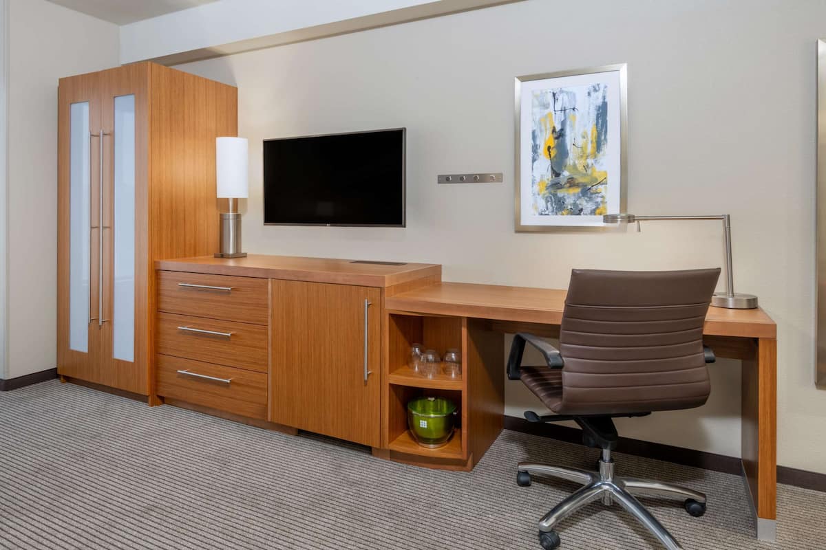 A hotel room with a wooden desk, a television, a painting, and a green bowl.