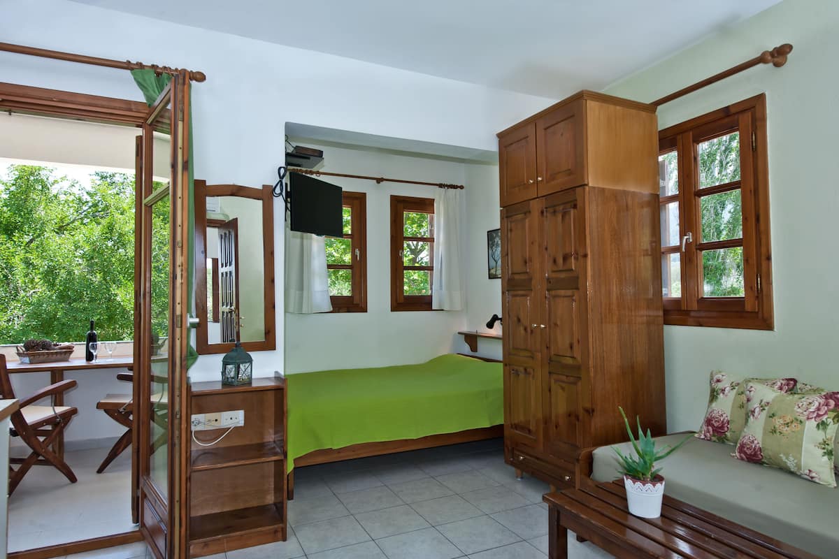 A bedroom with a bed, wooden wardrobe, a small table, a bench, and a window with curtains.