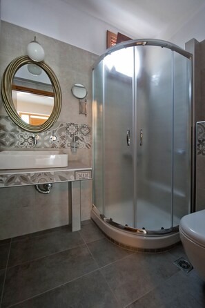 A modern bathroom with a glass-enclosed shower, a sink with a decorative mirror, and patterned wall tiles. - Sofia's House (Sithonia)