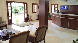 Un área de recepción con mostrador, sillas, un televisor y una planta en maceta.