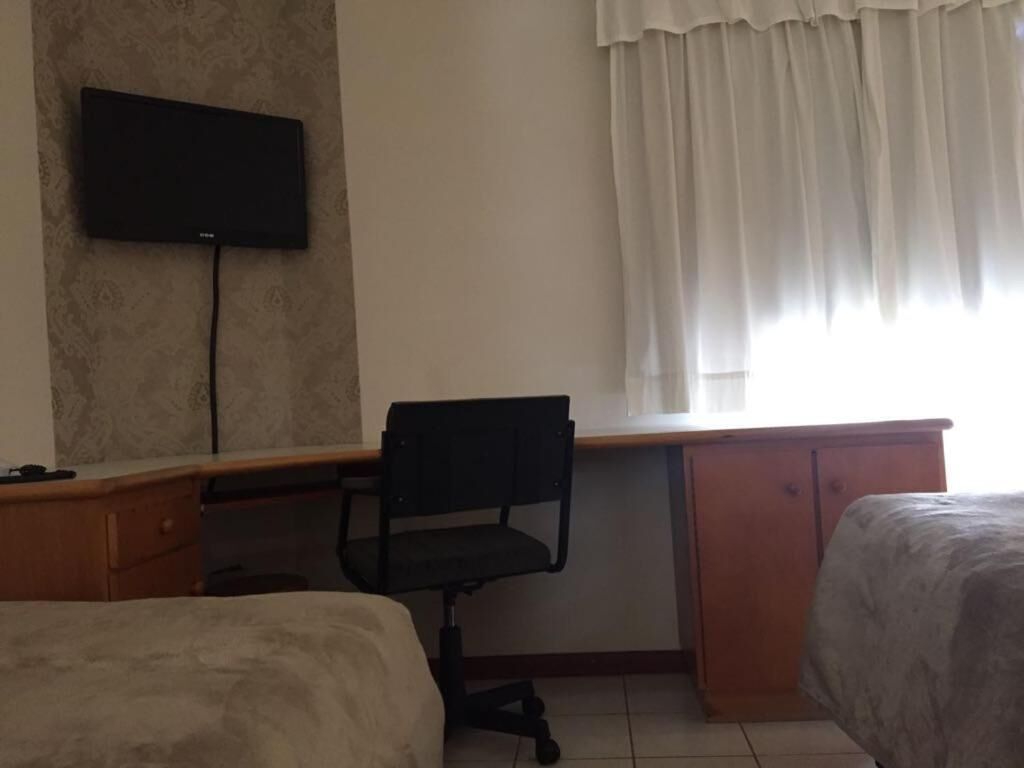 Habitación de hotel con cama, escritorio con silla, televisor montado en la pared y ventana con cortinas.