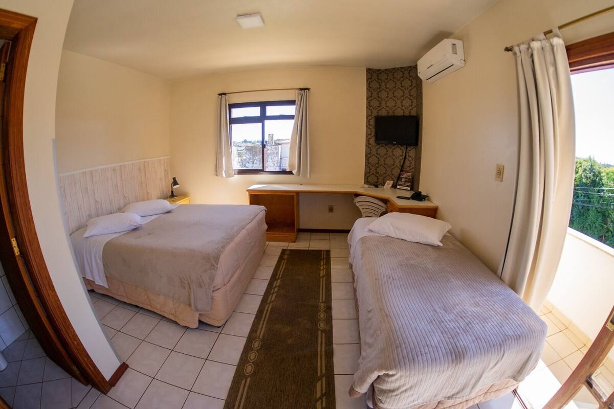 Una habitación con dos camas, un escritorio, una silla, un televisor y una ventana con cortinas.