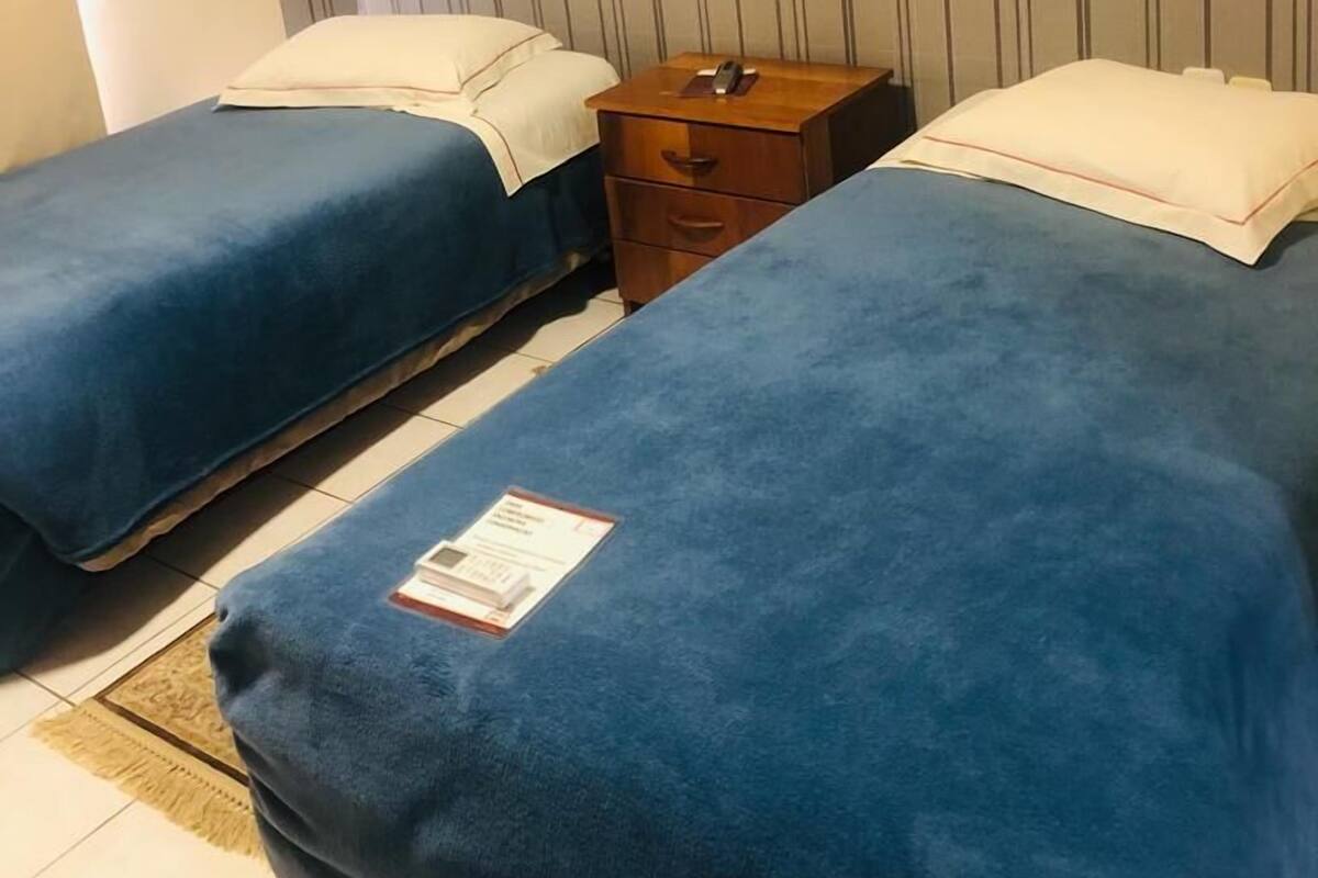 Habitación de hotel con dos camas individuales, una mesita de noche de madera y un aire acondicionado de pared.