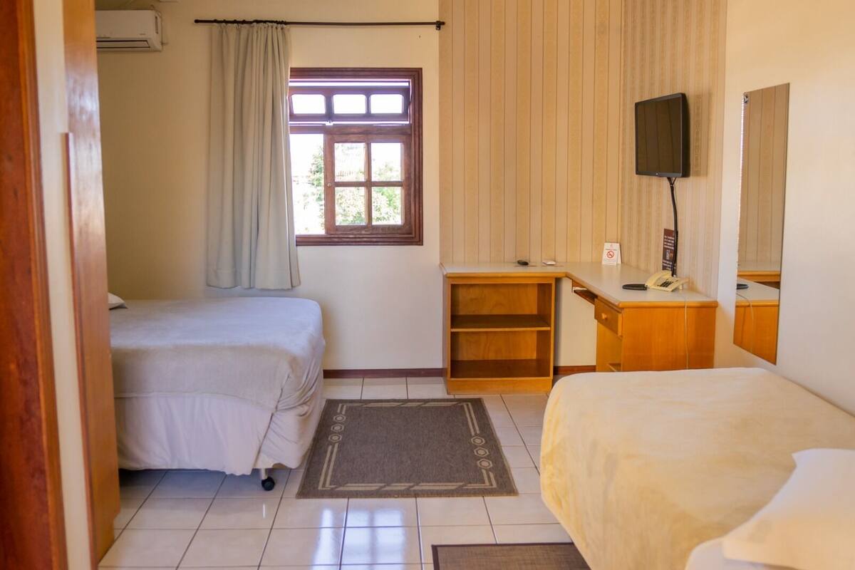 Habitación de hotel con dos camas, un escritorio, un televisor y un ventanal con cortinas.