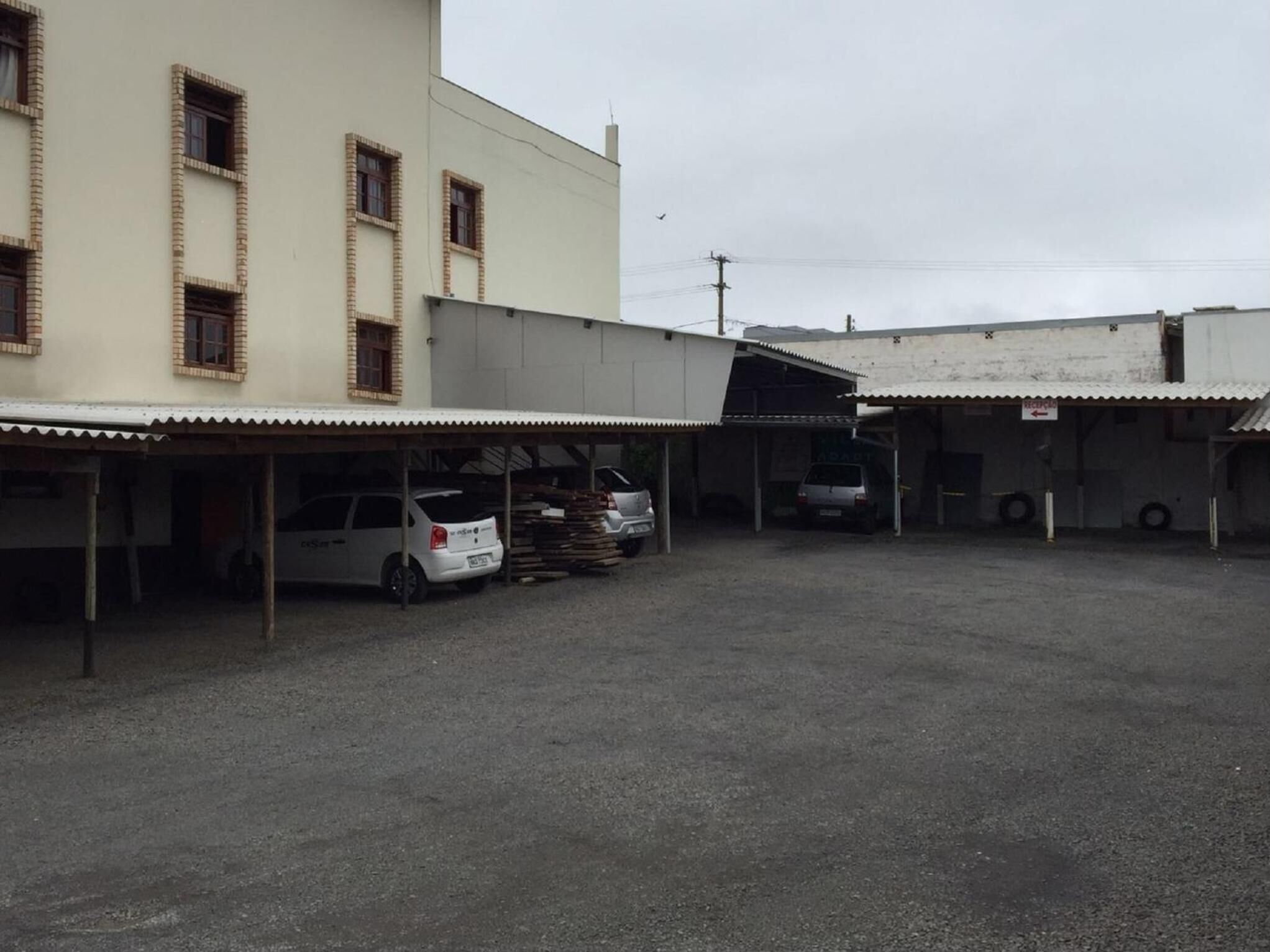 Um estacionamento com vários carros e um edifício com várias janelas e entrada coberta.