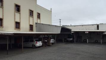 Um estacionamento com vários carros e um edifício com várias janelas e entrada coberta.