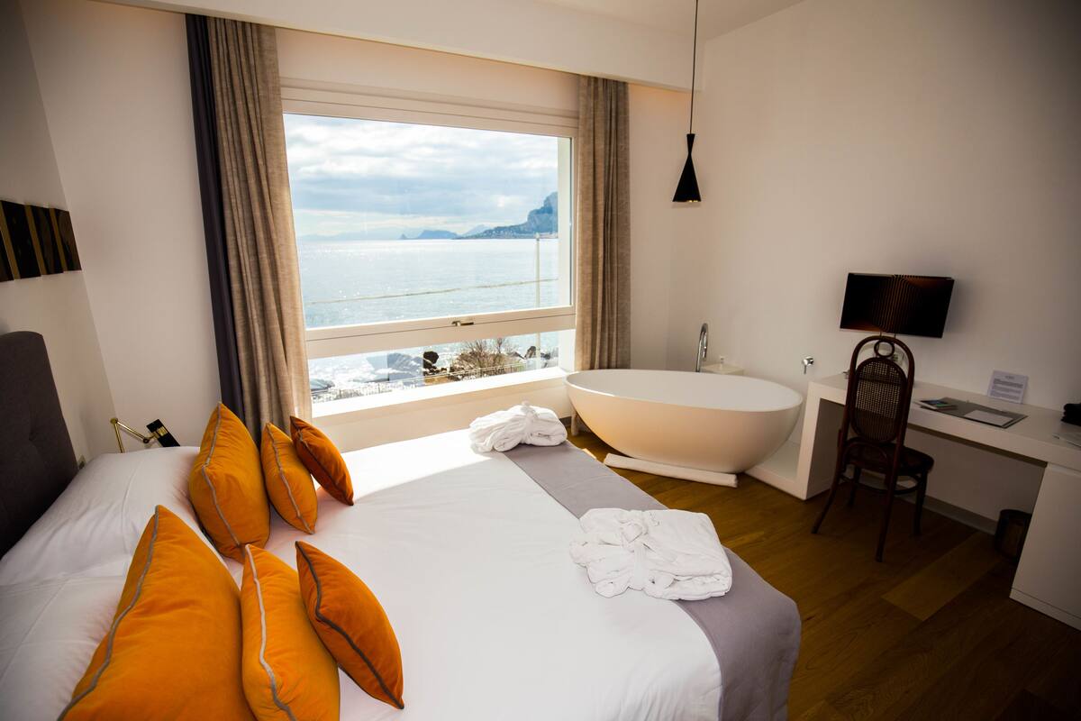 A hotel room with a large bed, a bathtub, a desk, and a view of the sea.