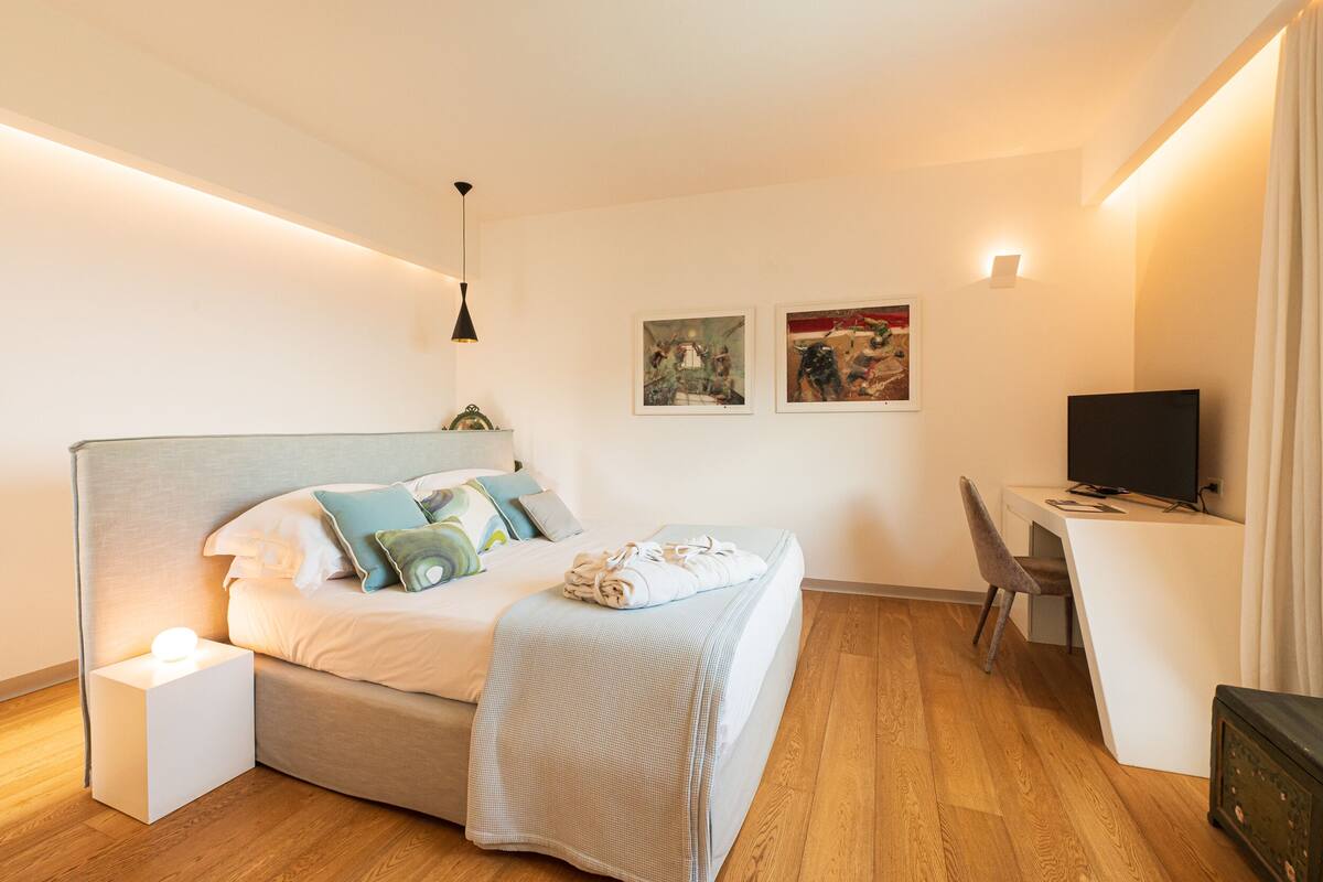 A modern bedroom with a bed, bedside table, desk, chair, and a television.