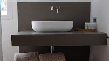 Une salle de bain moderne avec un grand lavabo sur pied, un miroir au-dessus, et deux serviettes ornées du motif « Unico ».
