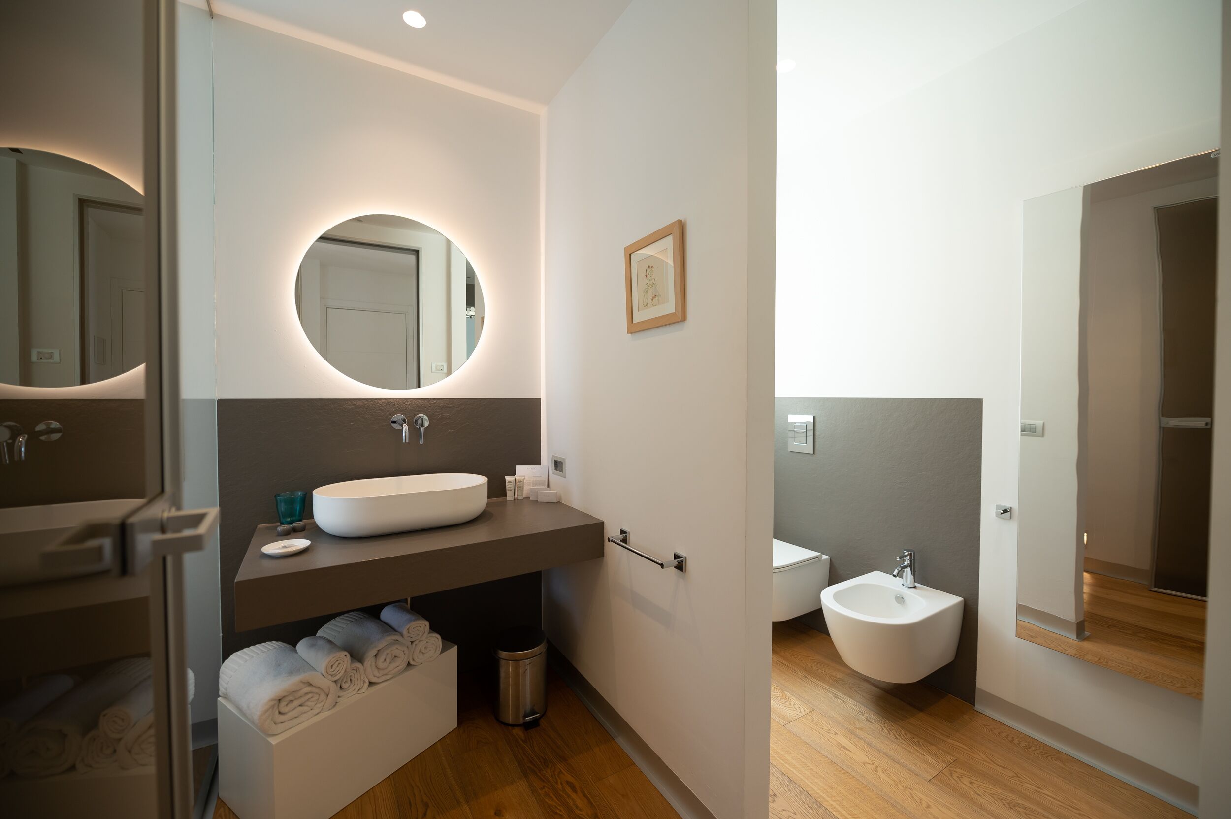 Un baño moderno con un espejo redondo, un lavamanos blanco, un bidé y un perchero.