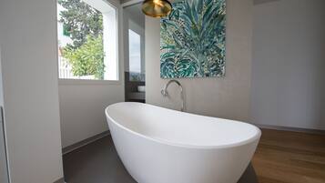 Une salle de bain moderne avec une baignoire sur pieds, une grande fenêtre et une œuvre d’art accrochée au mur.