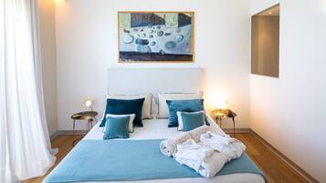 Ein ordentlich bezogenes Bett mit blauer Decke und Kissen, ein Gemälde darüber und Nachttischlampen.