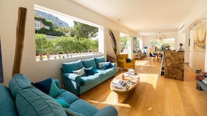 A modern living room with a blue sofa, wooden coffee table, and a view of a mountain and greenery outside.