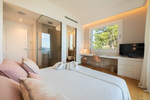 Una camera d'albergo moderna con un letto grande, una scrivania con televisore, una finestra vista alberi e bagno separato.