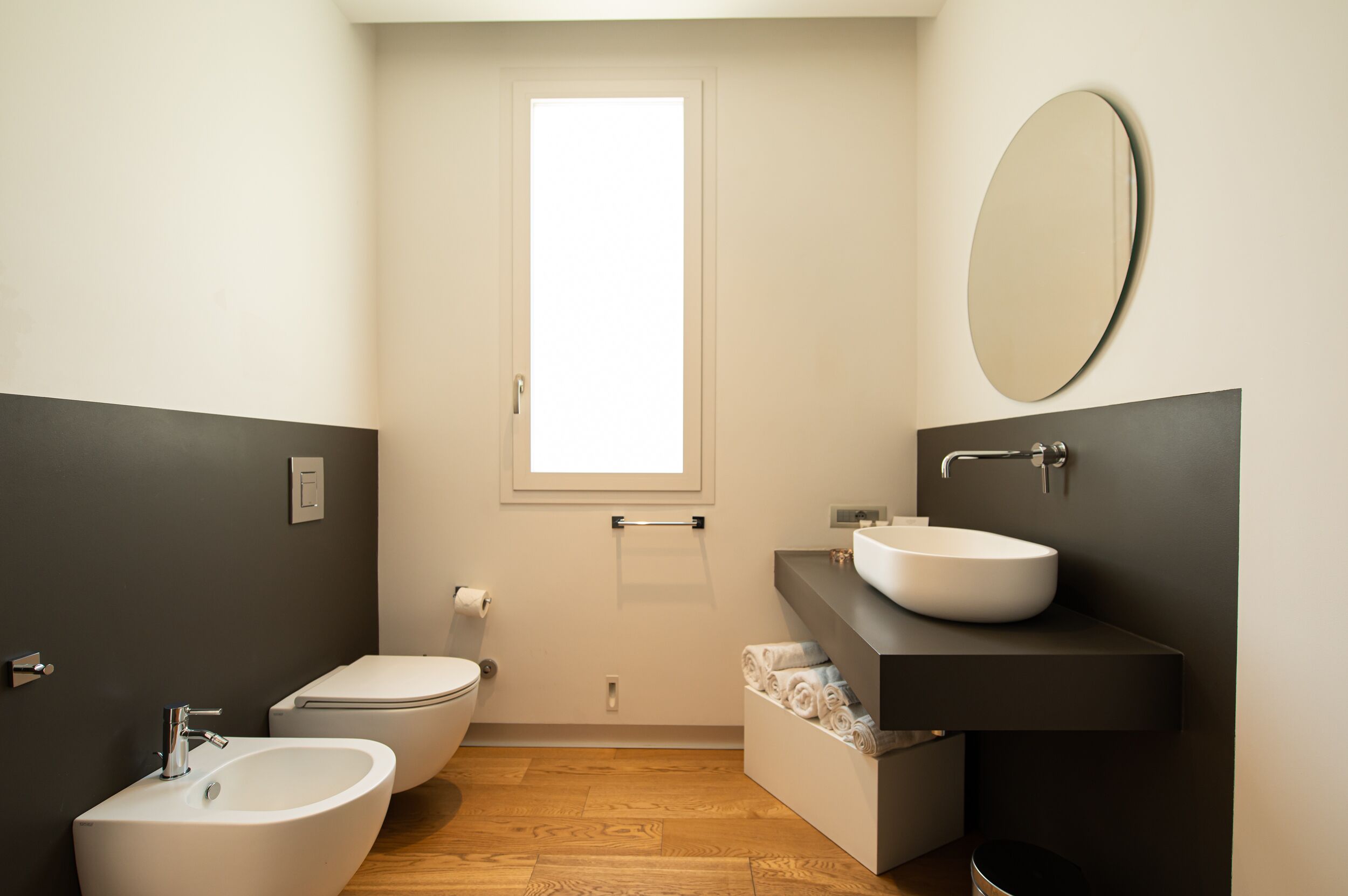 Un bagno moderno con bidet, WC e lavabo, dotato di uno specchio grande e una finestra.