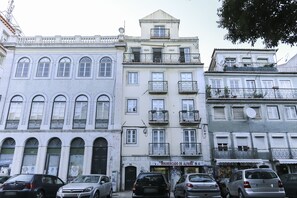 Filare di edifici a più piani con balconi, una vetrina visibile con insegne e auto parcheggiate lungo la strada.