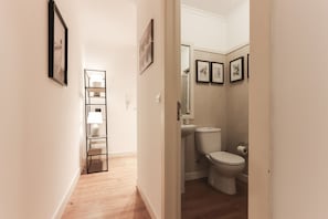 Un corridoio che porta a un bagno con il water, un lavandino e quadri appesi al muro.