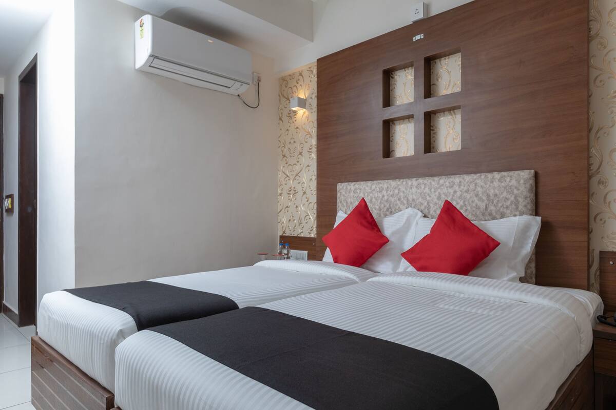 A double bed with white and black bedding, a wooden headboard with decorative panels, and an air conditioning unit on the wall.