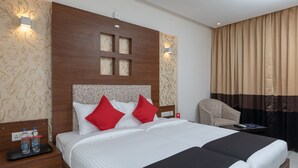 Ein Hotelzimmer mit einem großen Bett, zwei Nachttischen, einem Sessel und Blick ins Freie.