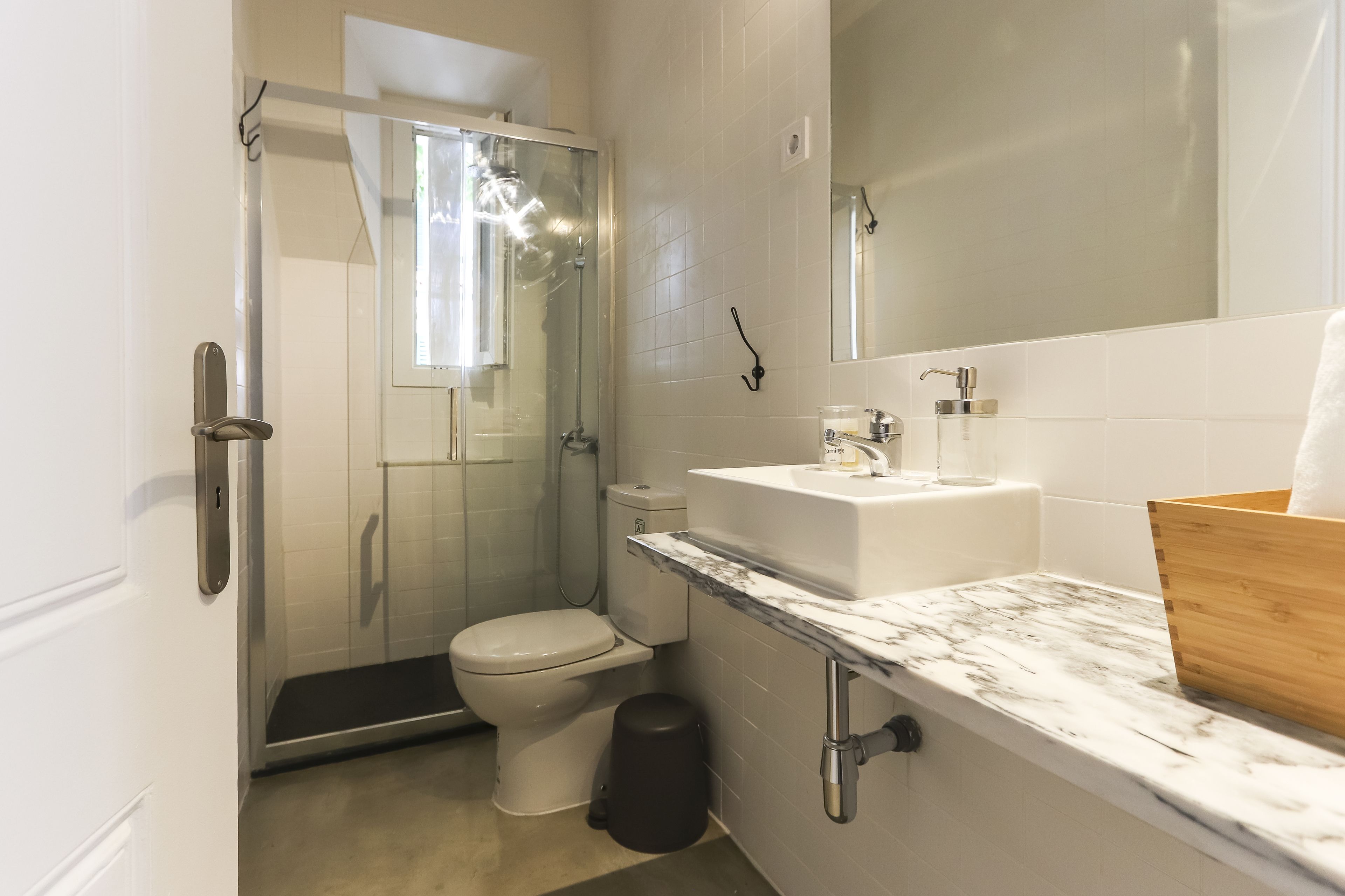 A modern bathroom with a glass-enclosed shower, a toilet, a sink with a marble countertop, and a wooden cabinet.