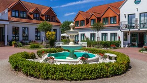 A courtyard with a central fountain, surrounded by neatly trimmed hedges and flower beds. - Hotelanlage Tarnewitzer Hof (Boltenhagen)