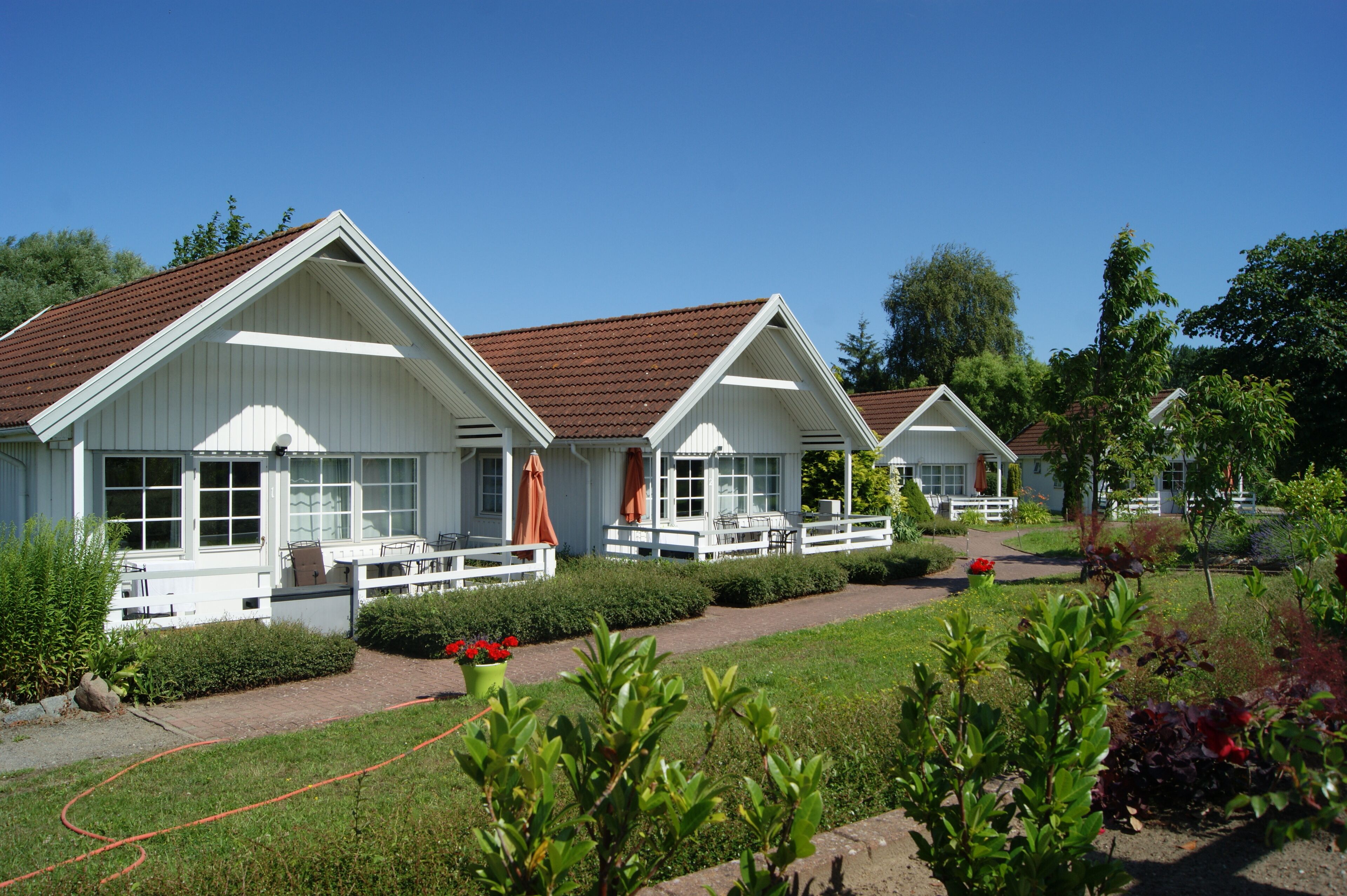 A row of white cabins with brown roofs, each with a porch and outdoor seating.