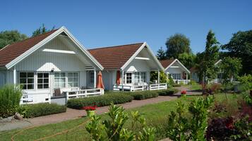 A row of white cabins with brown roofs, each with a porch and outdoor seating.