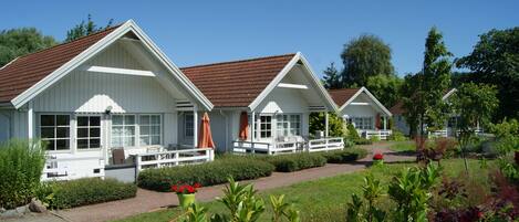 A row of white cabins with brown roofs, each with a porch and outdoor seating.
