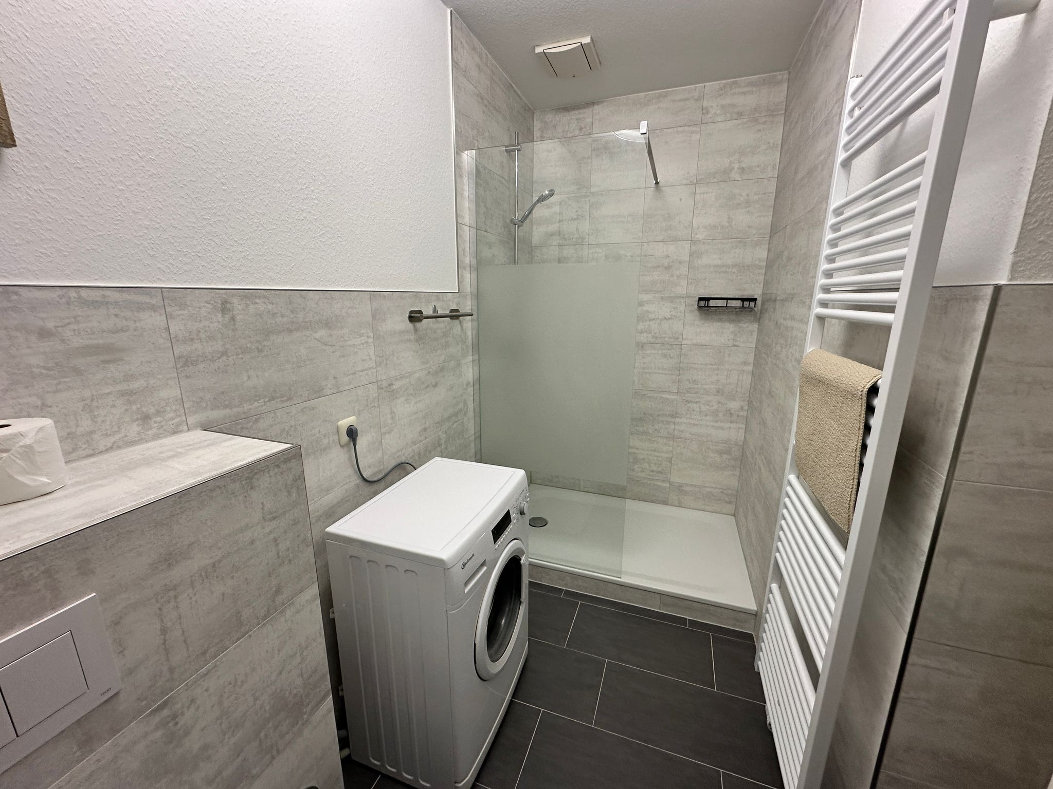 Un baño pequeño con lavadora, cabina de ducha de vidrio y un perchero para toallas.