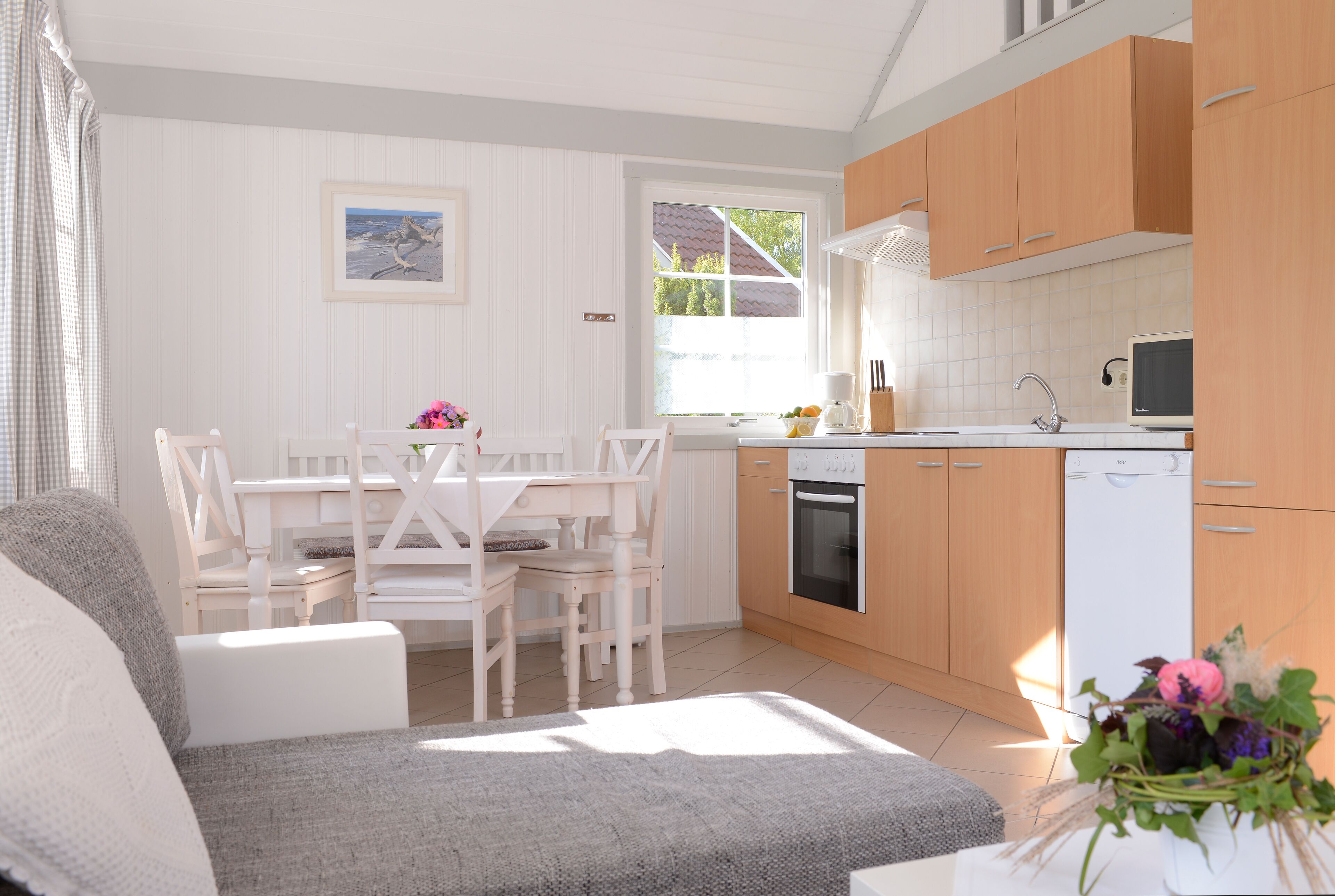 Une cuisine moderne avec des meubles blancs, un coin repas comprenant une table et des chaises blanches, et un canapé gris.