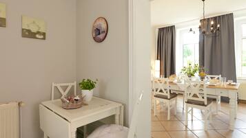 A dining area with a white table and chairs, a potted plant, and a clock on the wall.