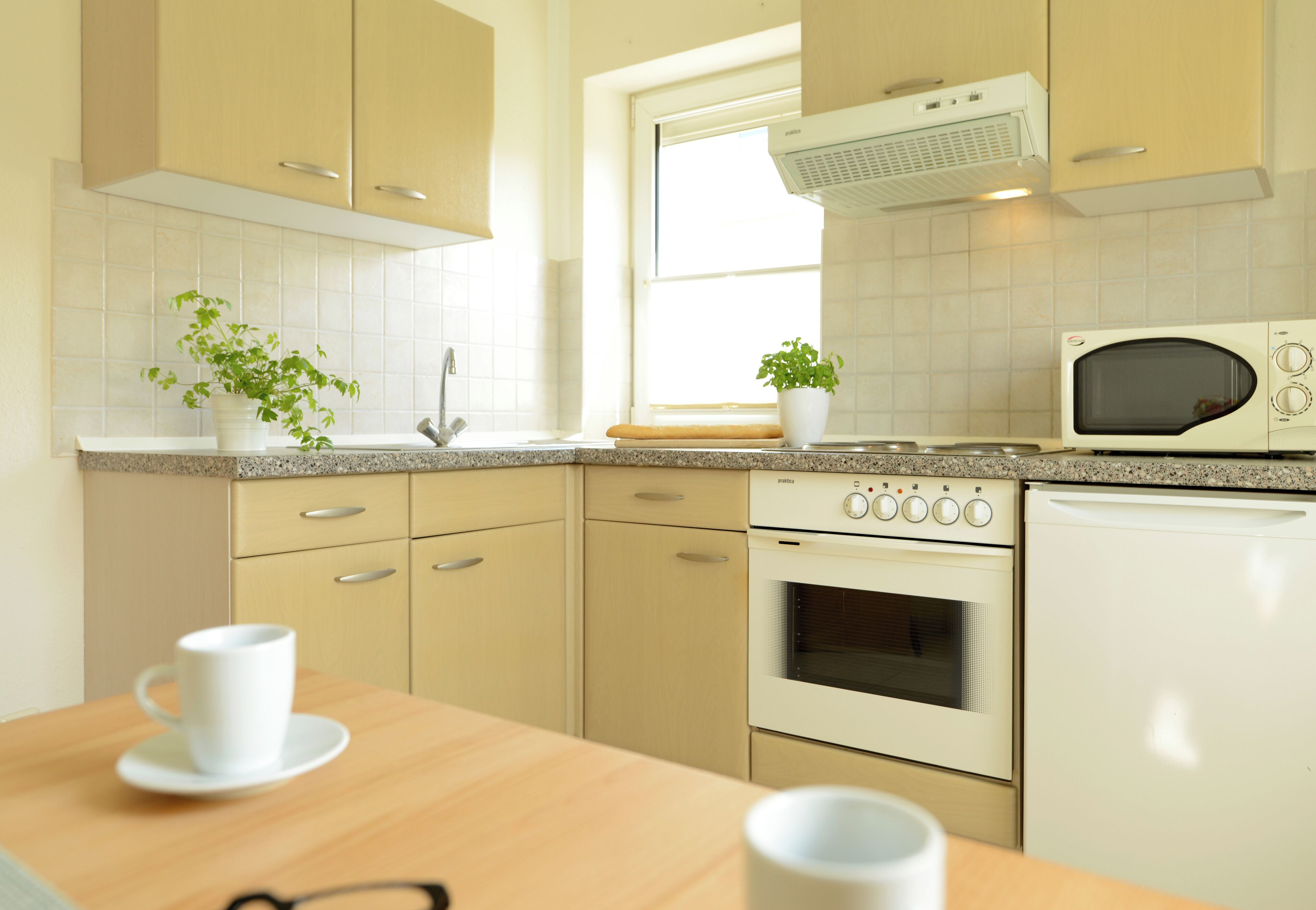 A modern kitchen with beige cabinets, a microwave, an oven, and a sink.