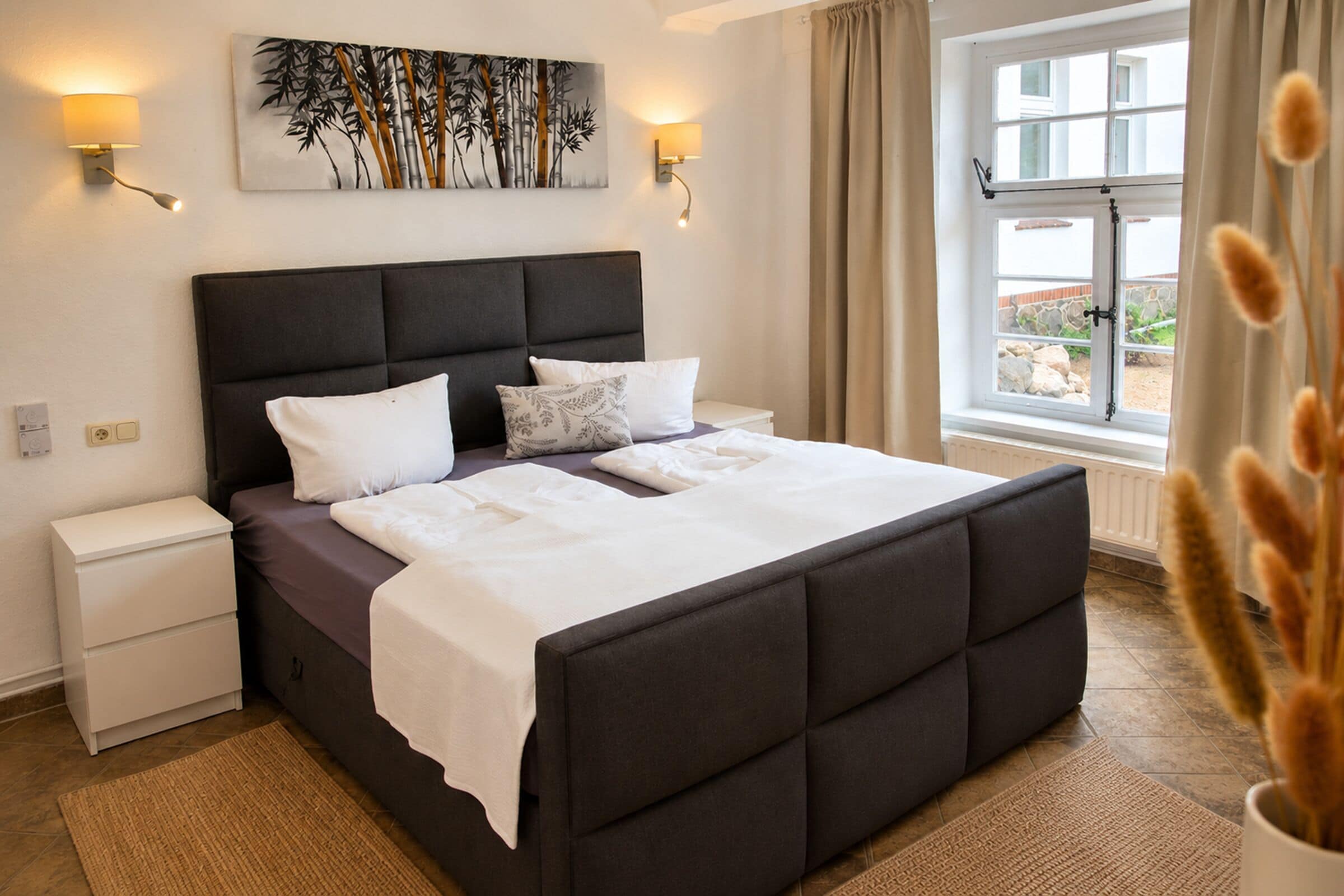 A bedroom with a large bed, bedside tables, a wall-mounted lamp, and a window with curtains.